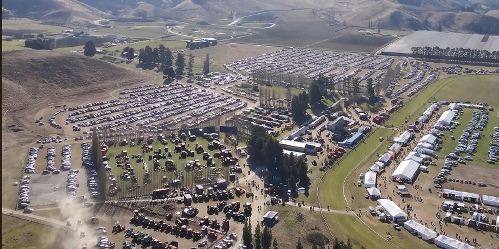 An aerial view of a Central Otago machinery show: rows of parked cars, machinery displays, trade marquees and the crowd spread across the grounds