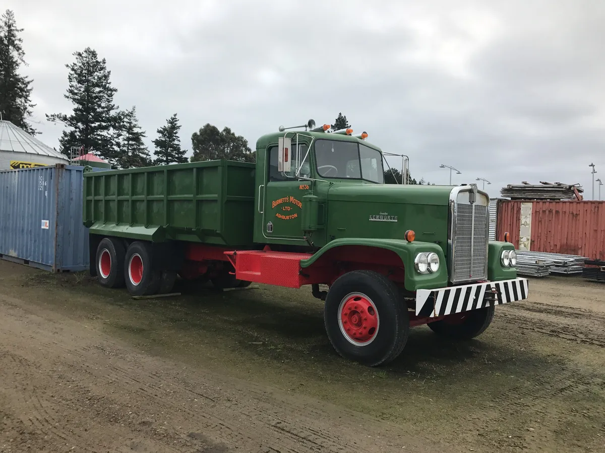 A green International tipper with a red chassis and black hoist body, parked on a yard
