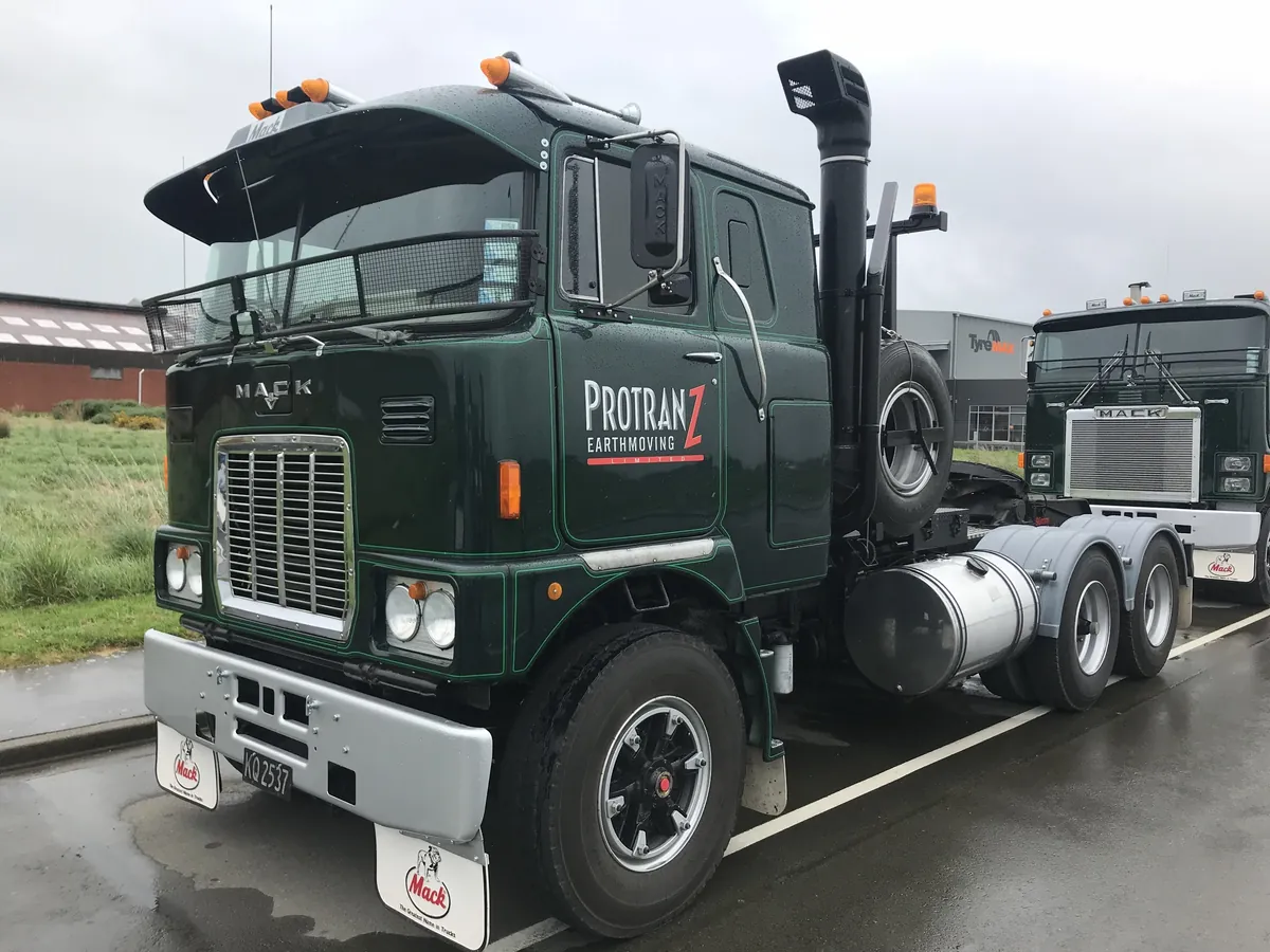 A dark green Mack cab-over tractor unit in Protranz Earthmoving livery, parked on wet concrete