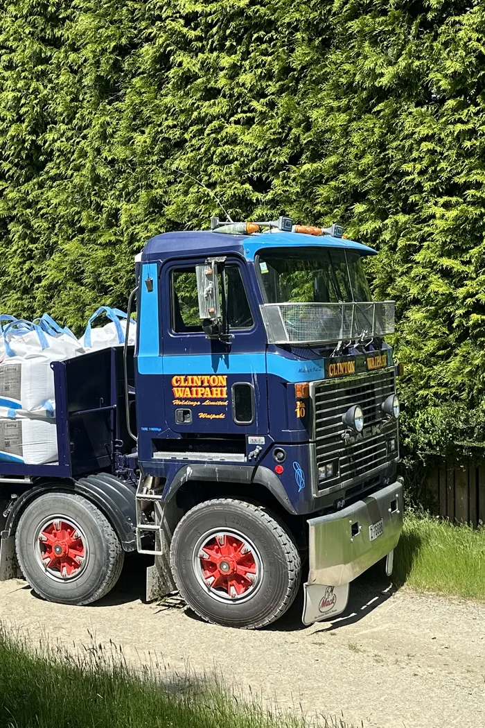 The same blue Mack loaded with fertiliser bags on a flatdeck, parked on a farm track