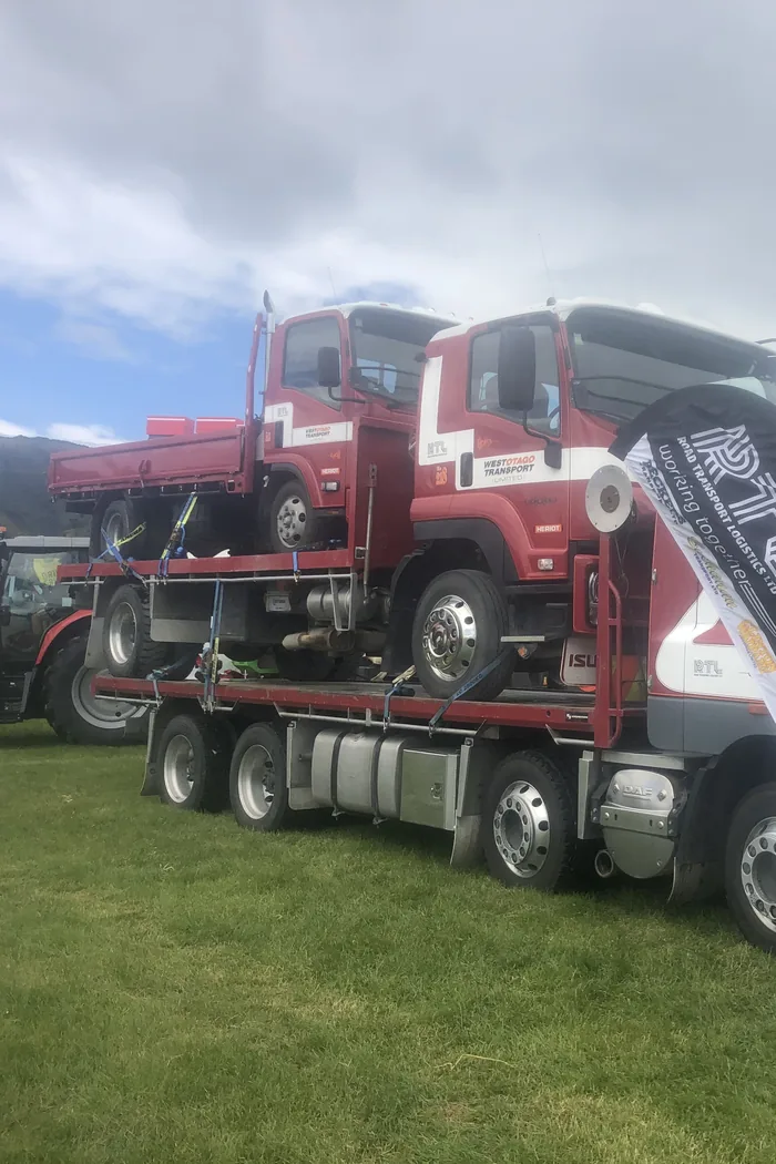 Two red Isuzu tippers stacked on the deck of a DAF transporter at an A&P show