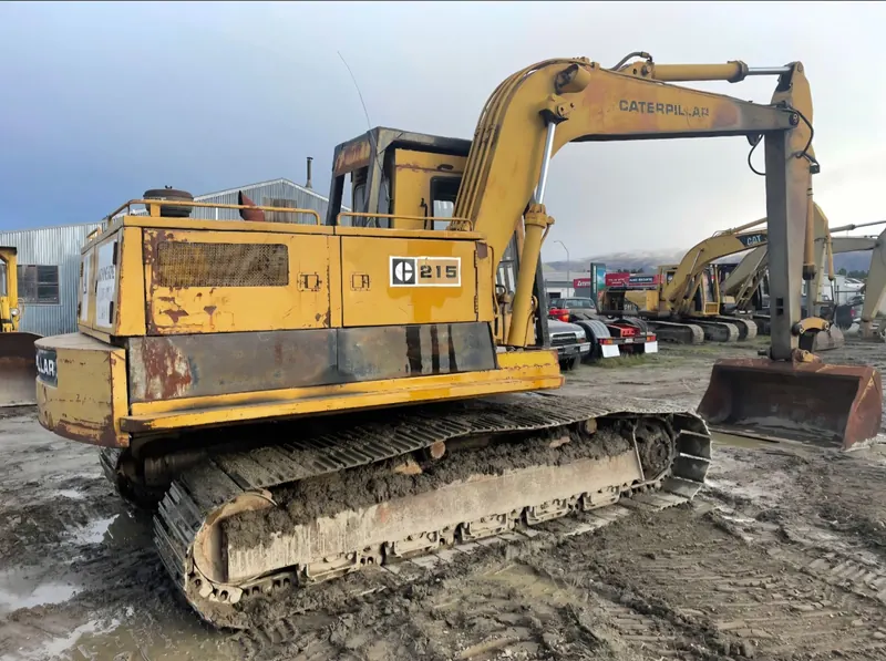 A yellow Caterpillar 215 excavator on a muddy yard