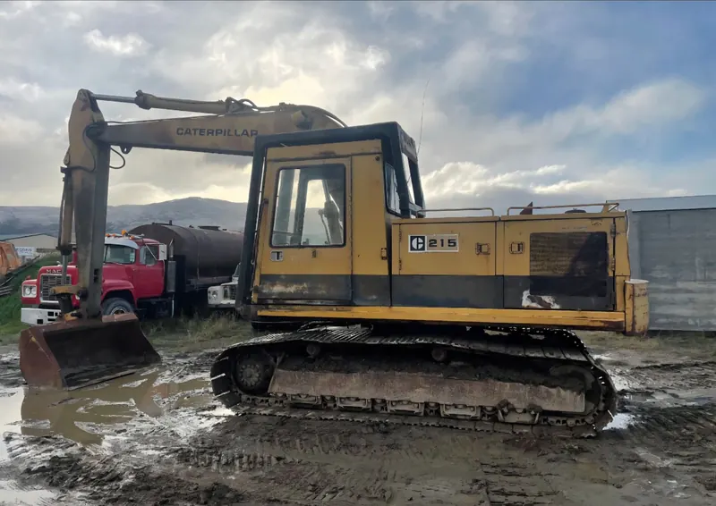 A Caterpillar 215 excavator side on, beside other machines