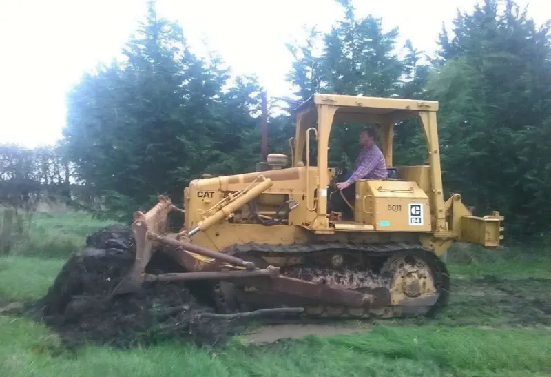 A Caterpillar D4E bulldozer on grass with pine trees behind