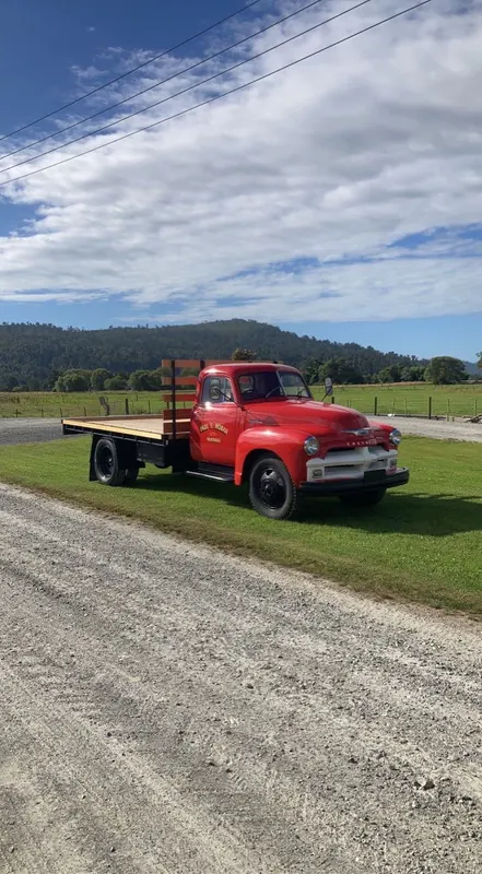 A red 1954 Chevrolet flatdeck truck on a gravel road