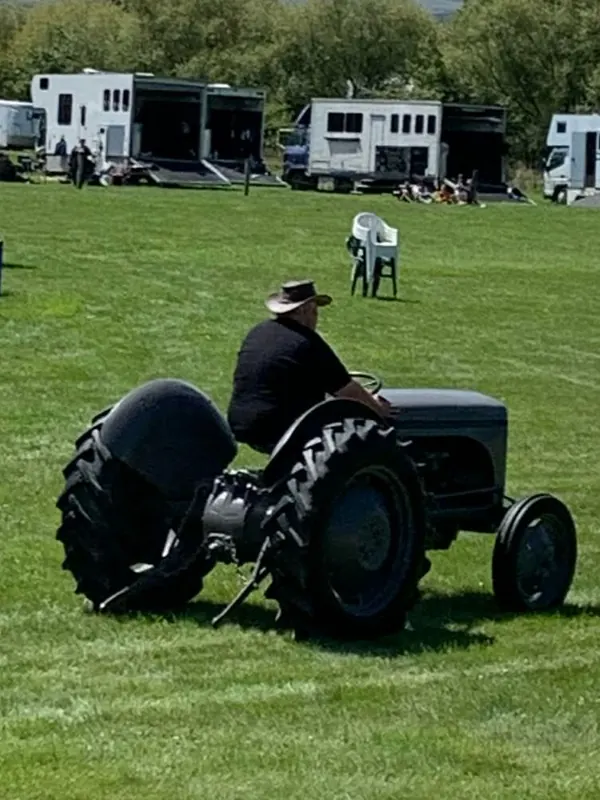 A man in a hat driving a black Ferguson TEA across a showground