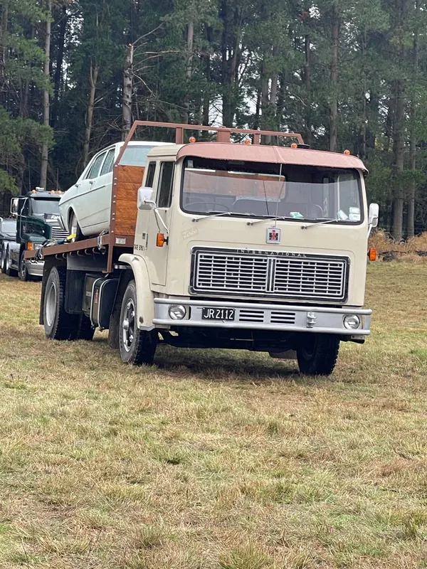 A cream International 1830B carrying a car on its deck