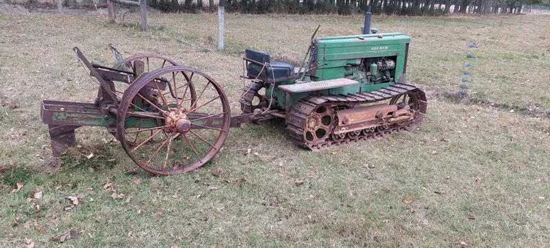 A green John Deere 40C crawler towing old farm implements