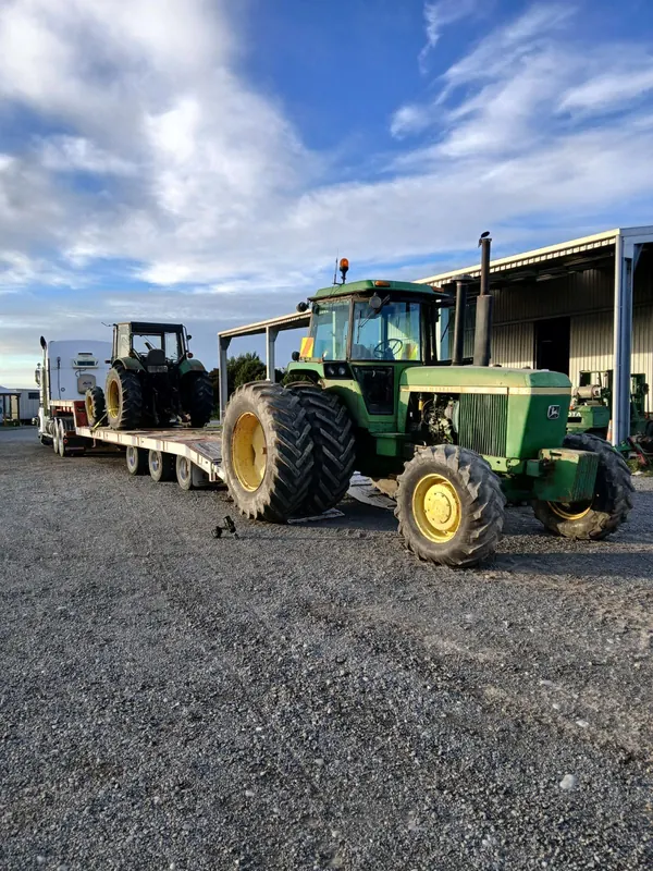 A John Deere 4630 beside a truck and transporter trailer