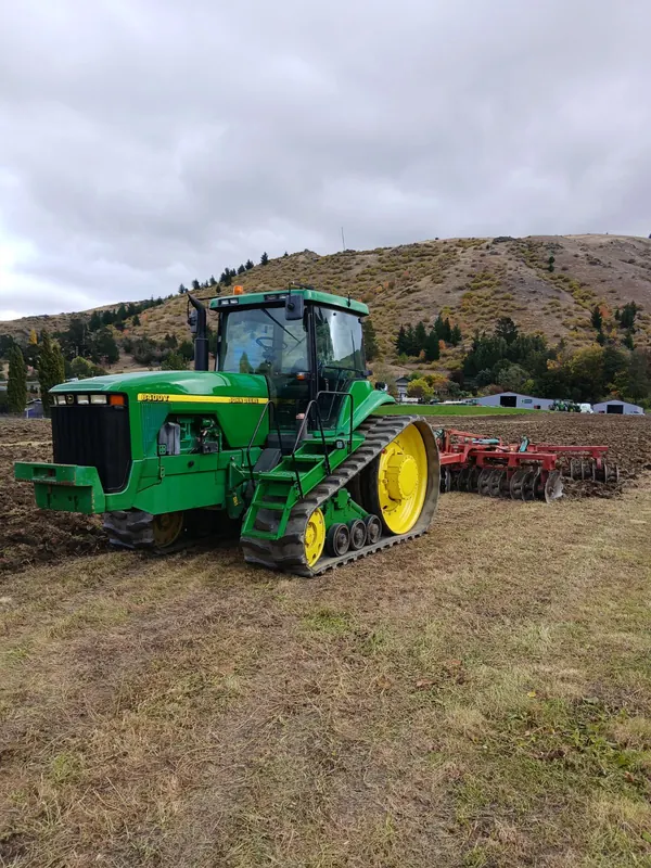 A tracked John Deere 8400T towing a cultivator on a hillside