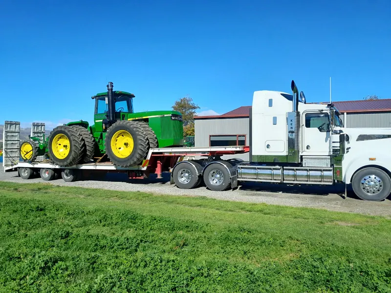 A big green John Deere 8850 loaded on a transporter behind a white truck