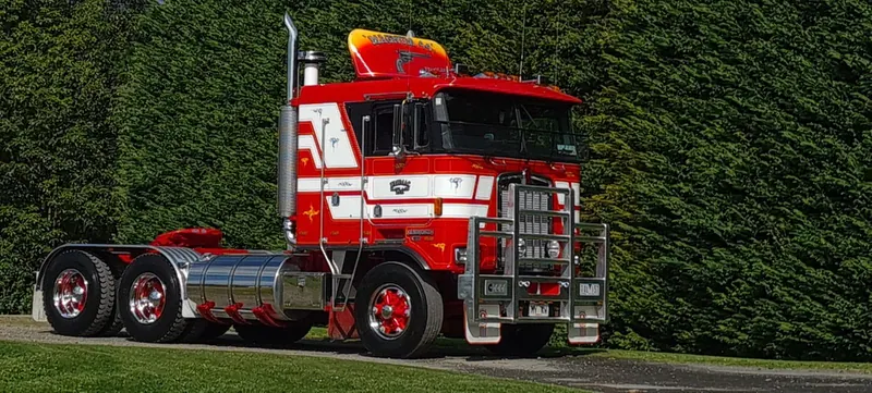 A red and white Kenworth K100E cab-over tractor unit