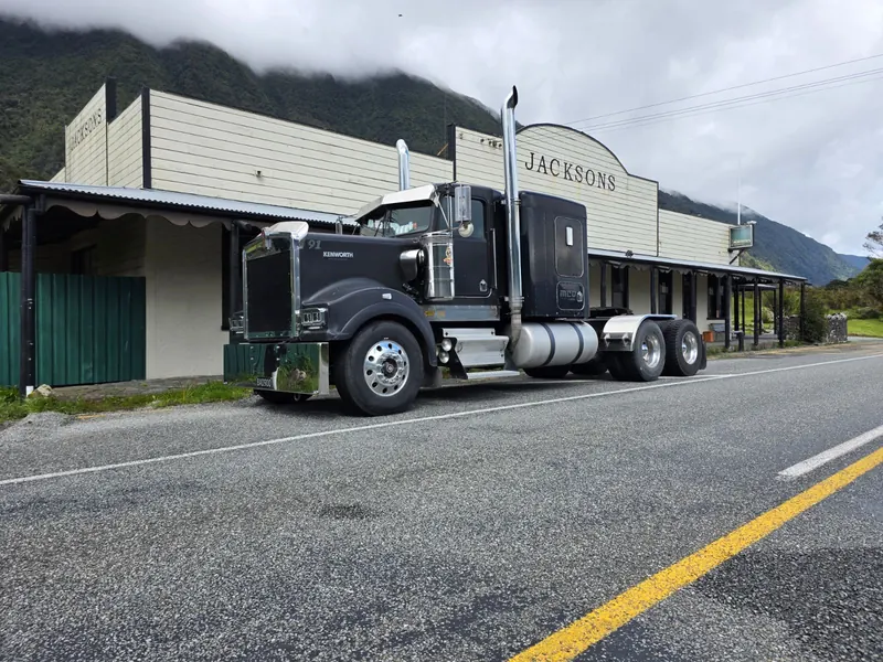 A black Kenworth T900 on a main street with hills behind