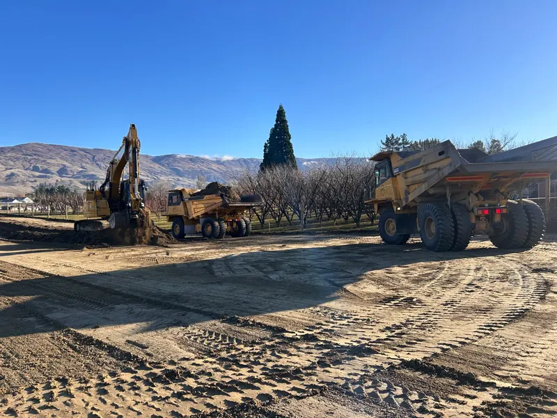 A Komatsu dump truck and an excavator on a dusty site with hills behind