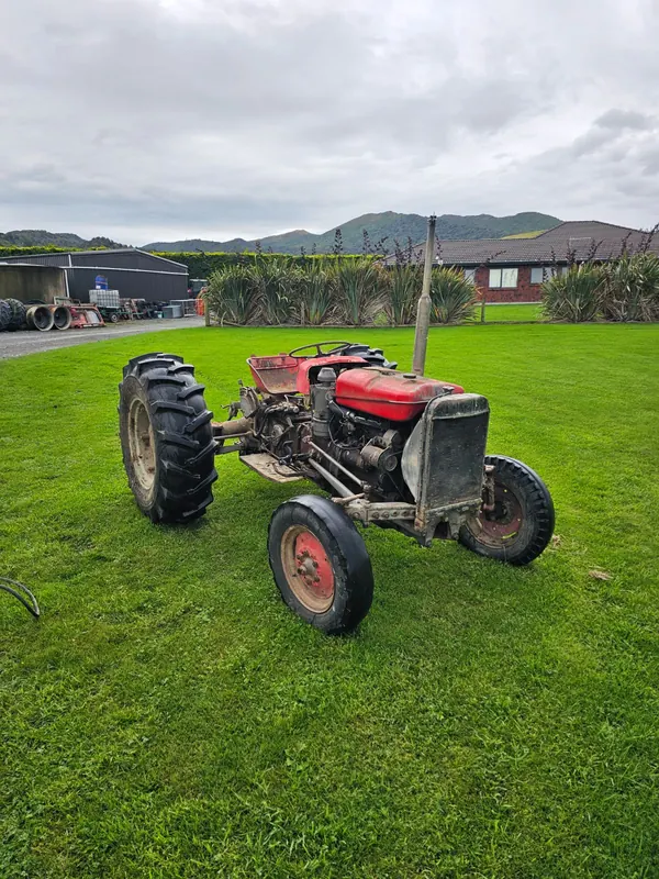 A red Massey Ferguson 135 on a green lawn with hills behind