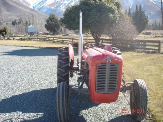 A red and grey Massey Ferguson 35 on a gravel drive with mountains behind