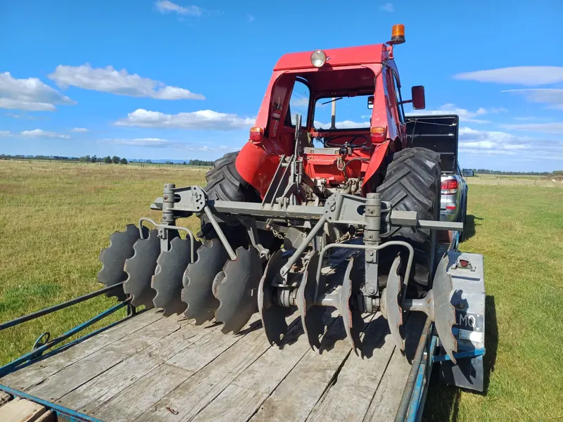 A red Massey Ferguson 35X with a disc harrow, loaded on a trailer