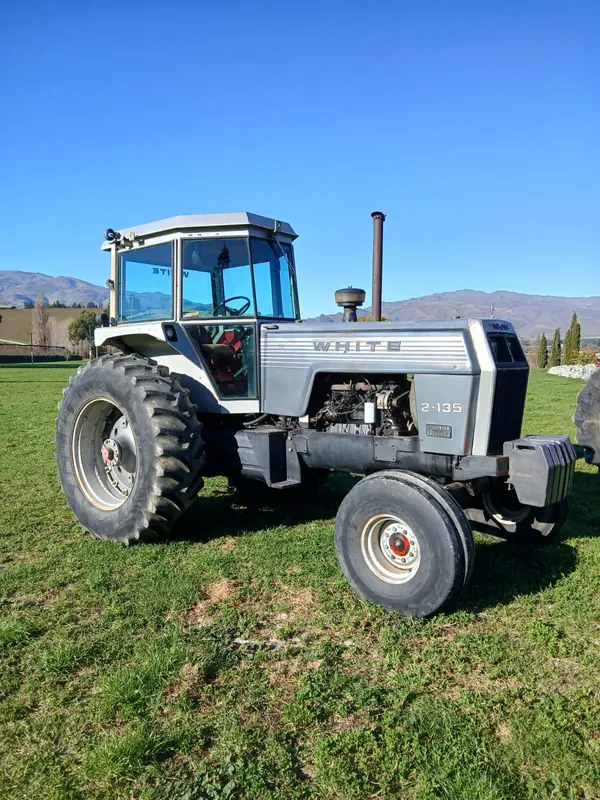 A silver White 2-135 Field Boss tractor on grass with hills behind