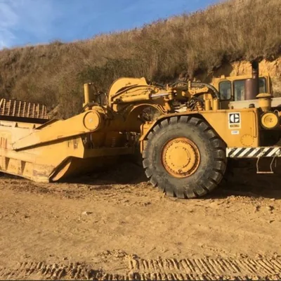 A yellow Caterpillar motor scraper working a cut face